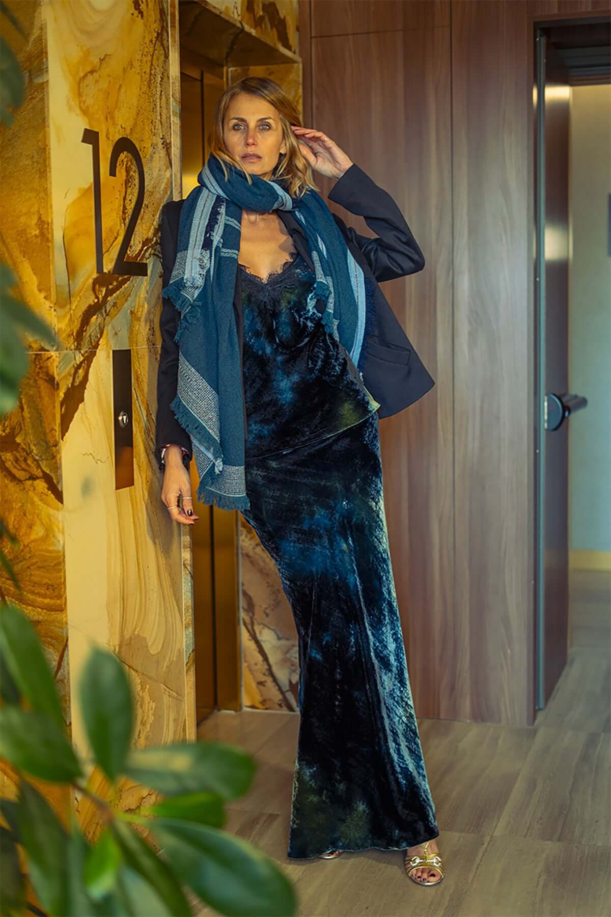 Model wearing a stylish Gonna Sbieco Velluto dress with a blazer and scarf in a modern interior setting.